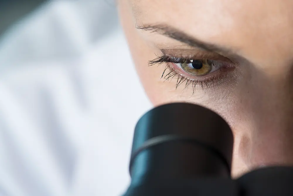 Žena koja jednim okom gleda kroz mikroskop