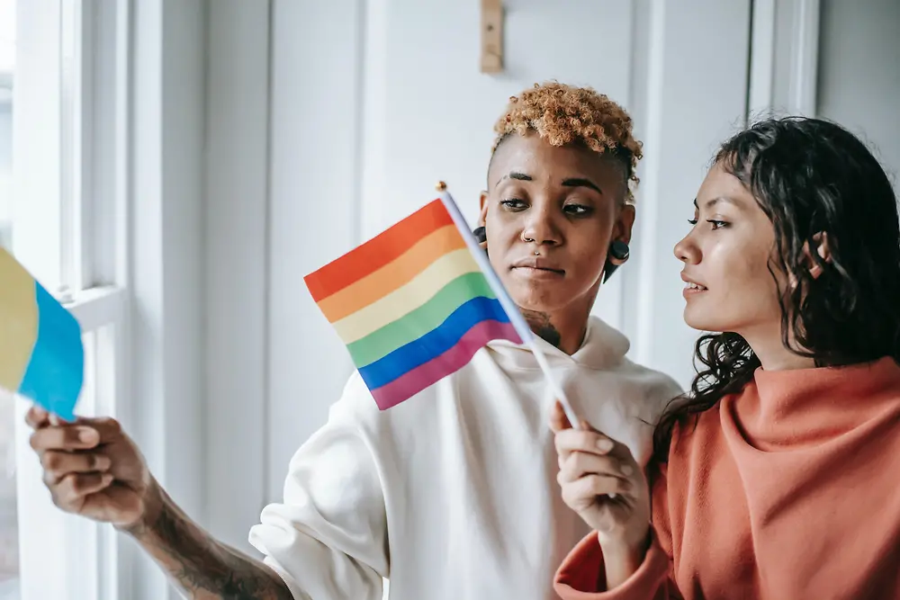 Dvije žene razgovaraju dok drže LGBTQ+ zastavu.