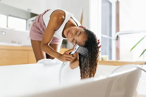 Žena u kupaonici pere svoju dugu smeđu kosu u kadi