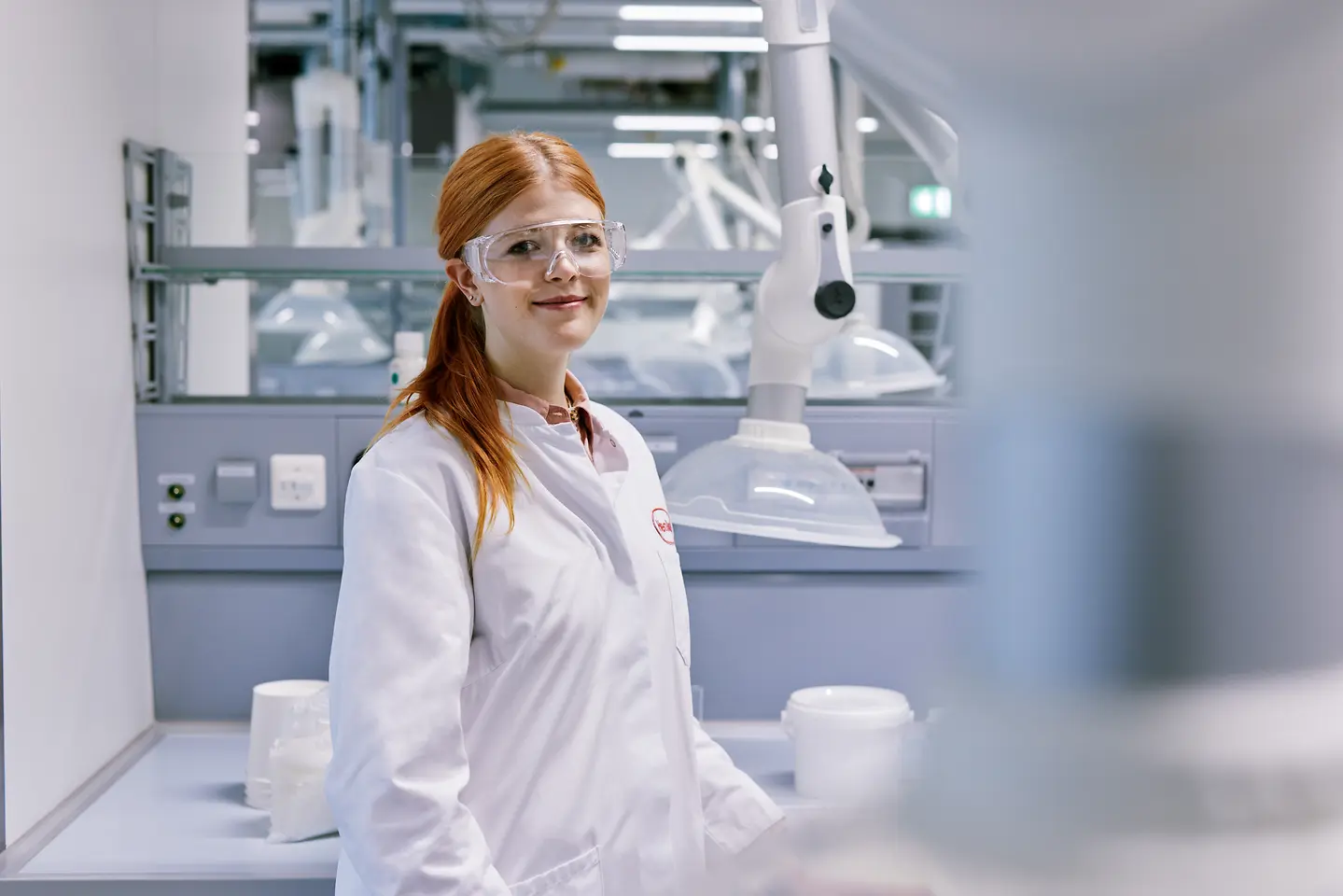 Diplomantica koja započinje karijeru u Henkelu, odjevena u bijeli laboratorijski ogrtač i stoji u modernom laboratorijskom okruženju s tehničkom opremom u pozadini.